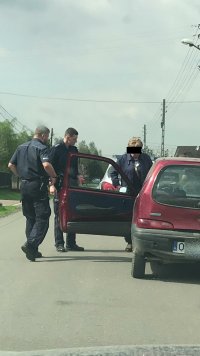Po prawej samochód marki Fiat Seicento, po lewej dwaj policjanci kontrolują starszego mężczyznę w peruce.