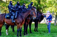 Policjanci na koniach i ojciec z dzieckiem na rękach - głaszczą konie