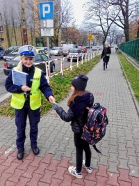 Policjantka na chodniku wręcza dziecku odblask.