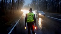 Policjant stoi na jezdni z dwoma czerwonymi latarkami