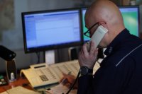 Policjant dyżurny rozmawia przez telefon, w tle monitory komputerowe.