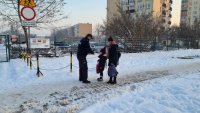 Policjant przed szkołą rozmawia z rodzicem i dzieckiem zmierzajacym na lekcje.