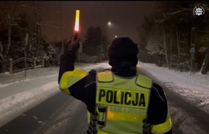 Policjant w zimowej scenerii, przed świtem zatrzymuje nadjeżdżający samochód.