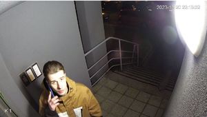Na zdjęciu młody mężczyzna przed drzwiami klatki schodowej.