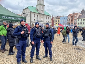 Na zdjęciu pozuje trzech mundurowych policjantów stojących na tle gliwickiego rynku pełnego ludzi.