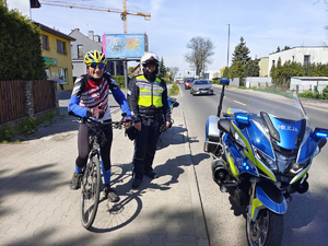 Na zdjęciu po lewej uśmiechnięty rowerzysta, obok niego policyjny motocyklista i zaparkowany motocykl. Pozują do zdjęcia z zadowolonym rowerzystą.